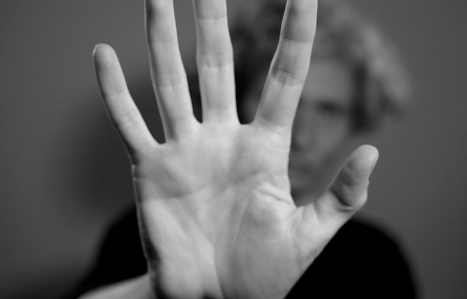 Black and white image with hand filling the screen, face is visible out of focus and in background