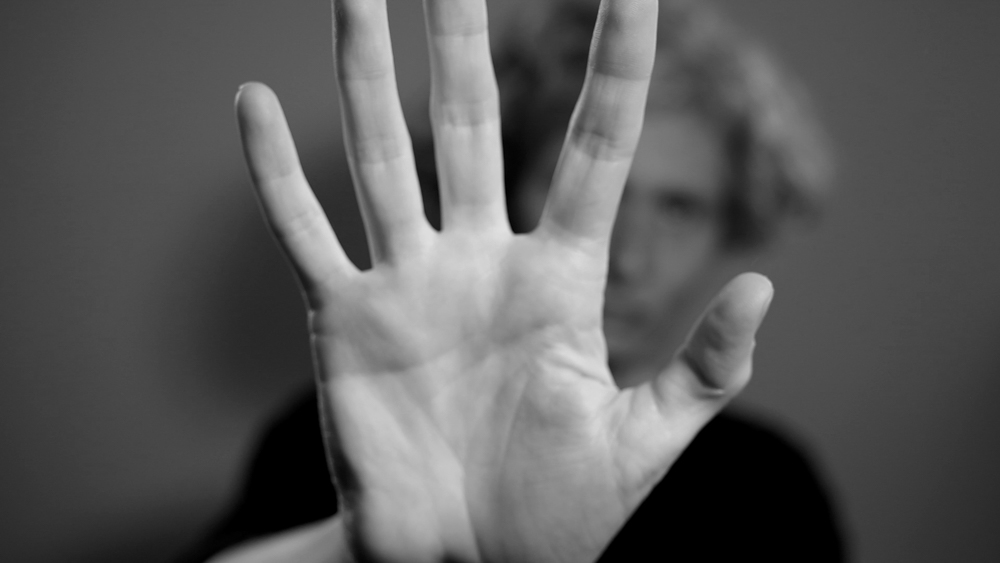 Black and white image with hand filling the screen, face is visible out of focus and in background